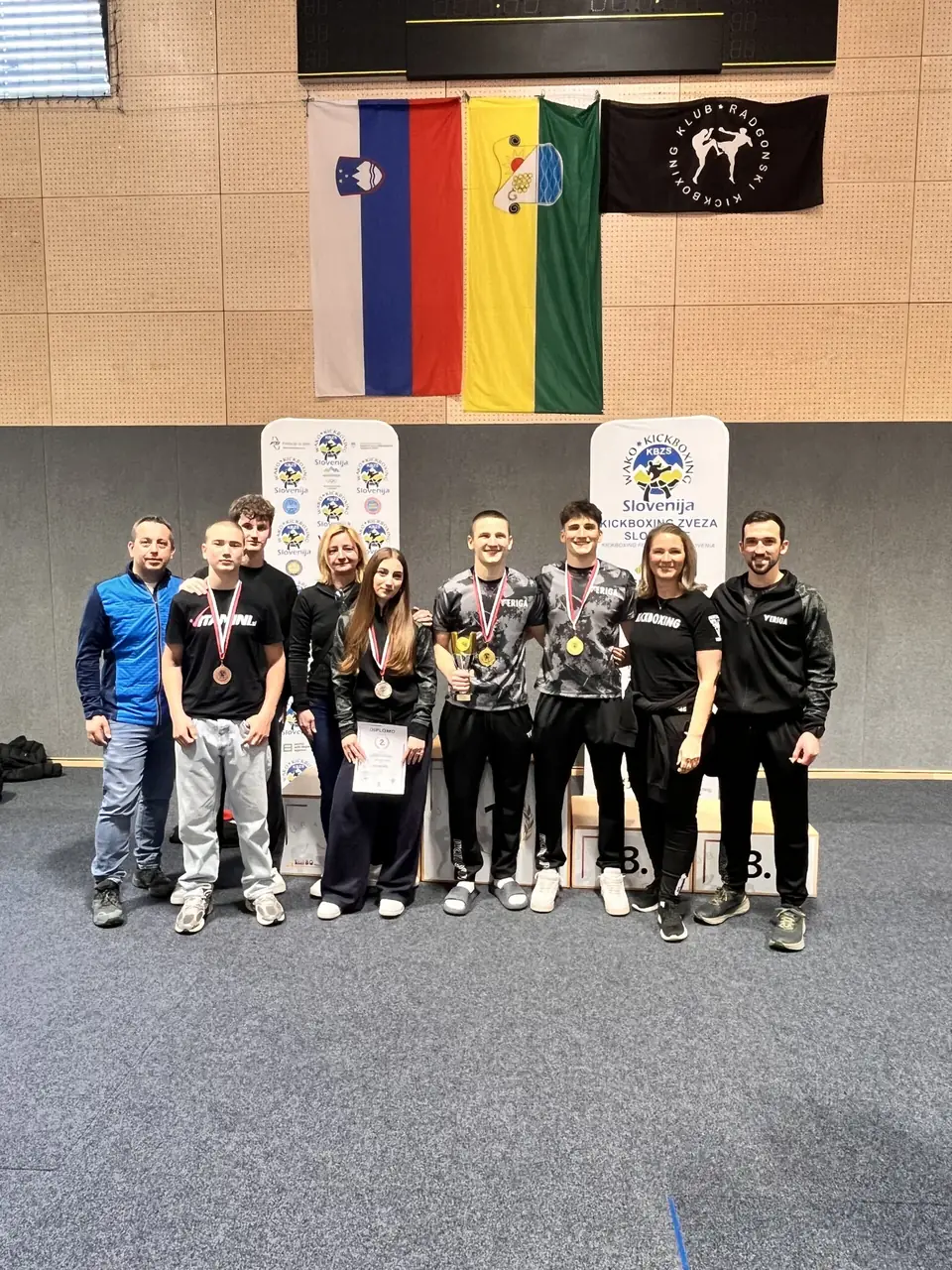 Skupina tekmovalcev z medaljami v telovadnici z zastavami